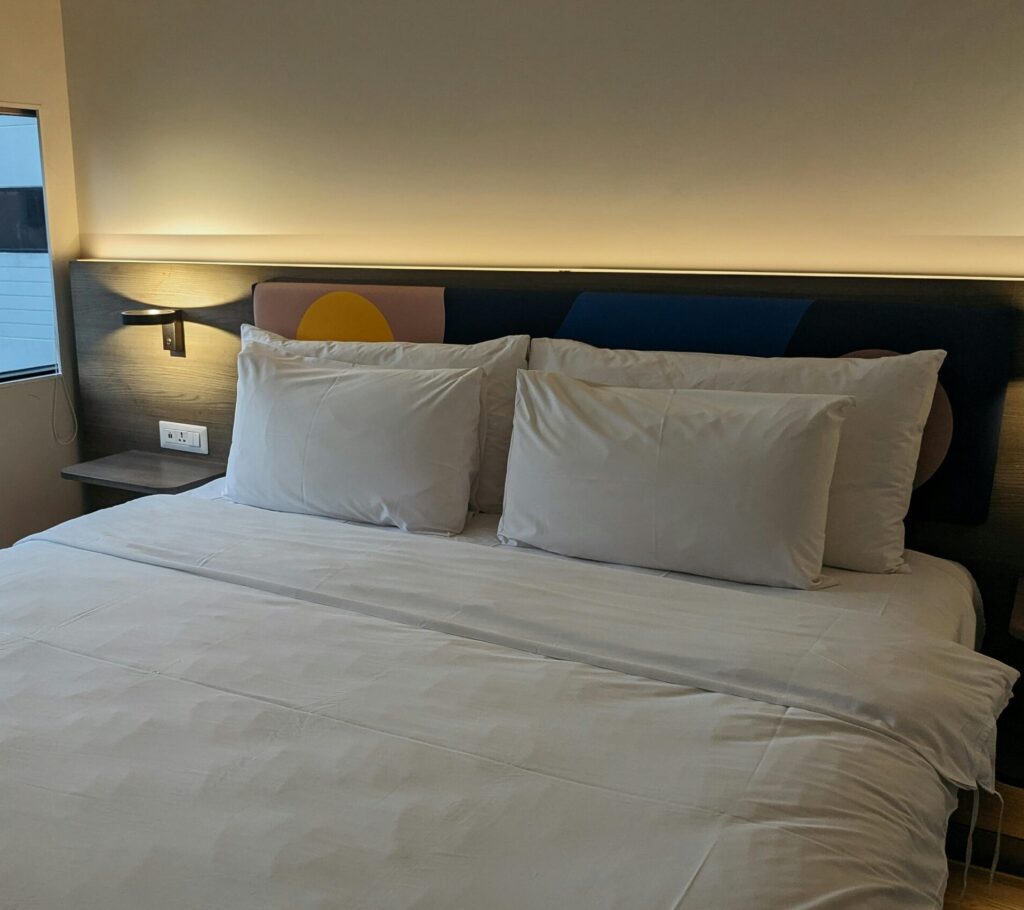 A cozy and modern hotel room featuring a neatly made bed with white linens and a view from the window.