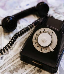 Classic black rotary phone placed atop scattered dollar bills, evoking a retro financial vibe.