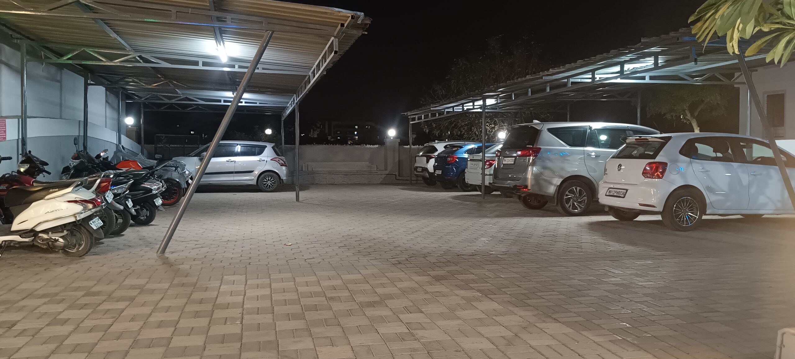 Covered parking shed at Shivrudra Hotel with parked bikes and cars for event guests and room stay visitors.